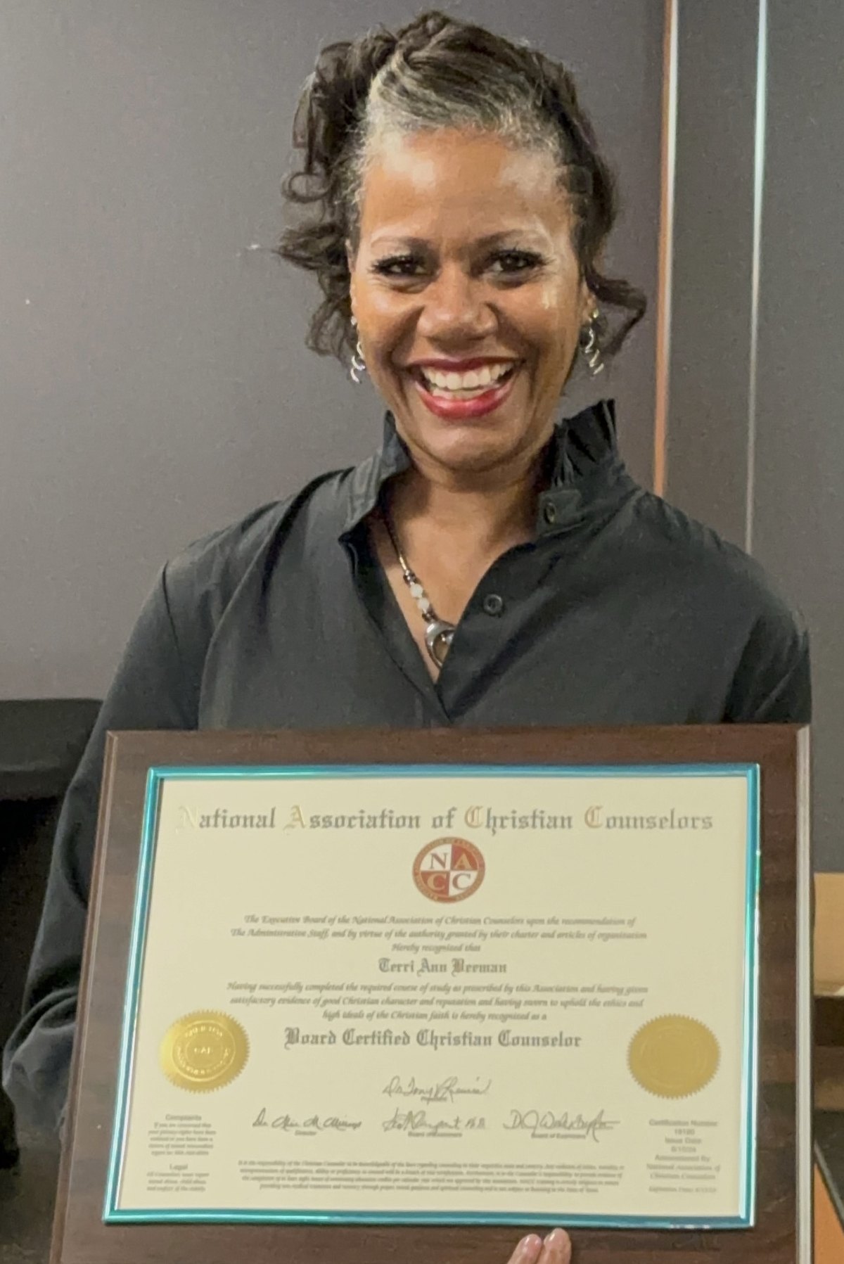 Terrie Beeman smiling while holding her Board Certified Christian Counselor certificate
